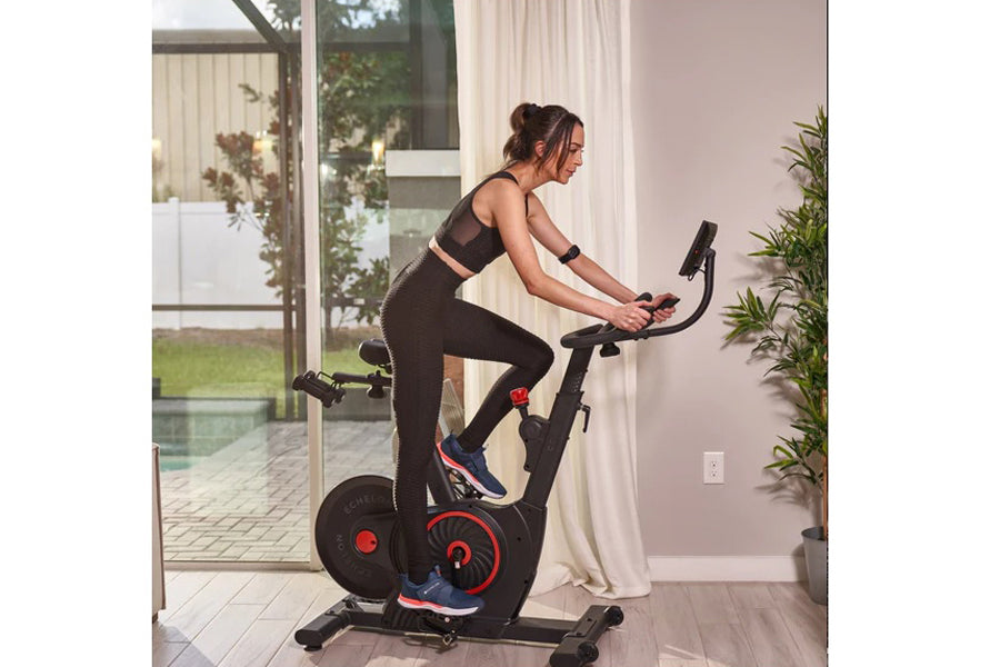 Woman in black sports bra and leggings riding black and red stationary exercise bike indoors