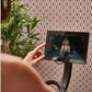 Person's hand on Echelon Smart Connect Bike EX-5s-10 with tablet displaying fitness class, potted plant visible