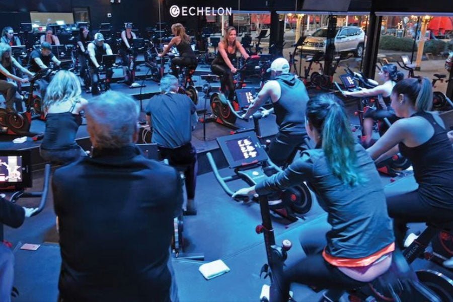 Group fitness class with multiple participants on black and red stationary bikes in Echelon studio with instructor leading wo