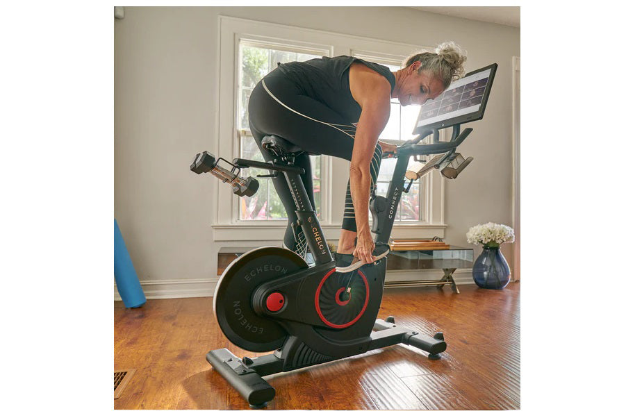 Man using black Echelon Connect stationary bike with red accents and tablet display in home gym setting