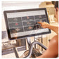 Person using touchscreen display on Echelon Smart Connect Bike EX-5s-22 showing workout class grid interface