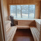 Interior of wooden sauna with light pine benches, metal heater basket, large windows overlooking winter landscape
