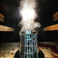 Harvia Cilindro electric sauna heater with white metal cage design, producing steam vapor, shown in sauna room setting