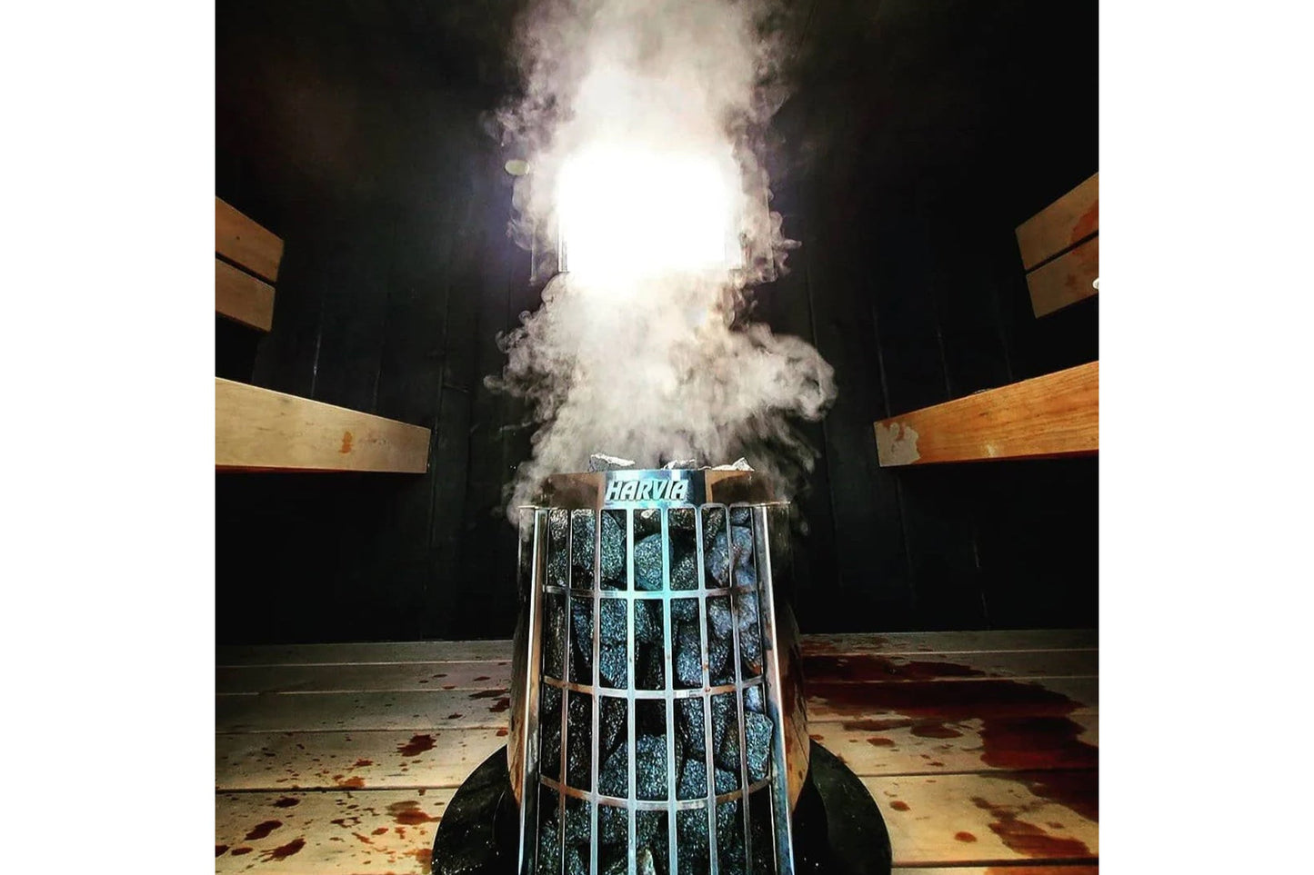 Harvia Cilindro electric sauna heater with white metal cage design, producing steam vapor, shown in sauna room setting