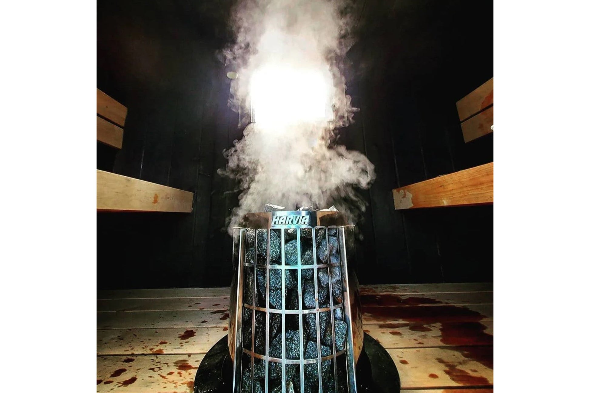 Harvia Cilindro electric sauna heater with white metal cage design, producing steam vapor, shown in sauna room setting