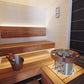 Modern sauna interior with wooden benches, stainless steel and leather sauna heater bucket, and light wood paneling on walls