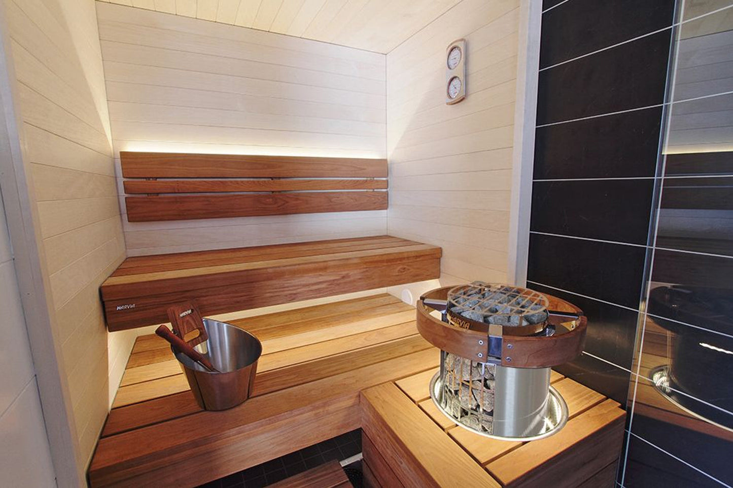 Modern sauna interior with wooden benches, stainless steel and leather sauna heater bucket, and light wood paneling on walls