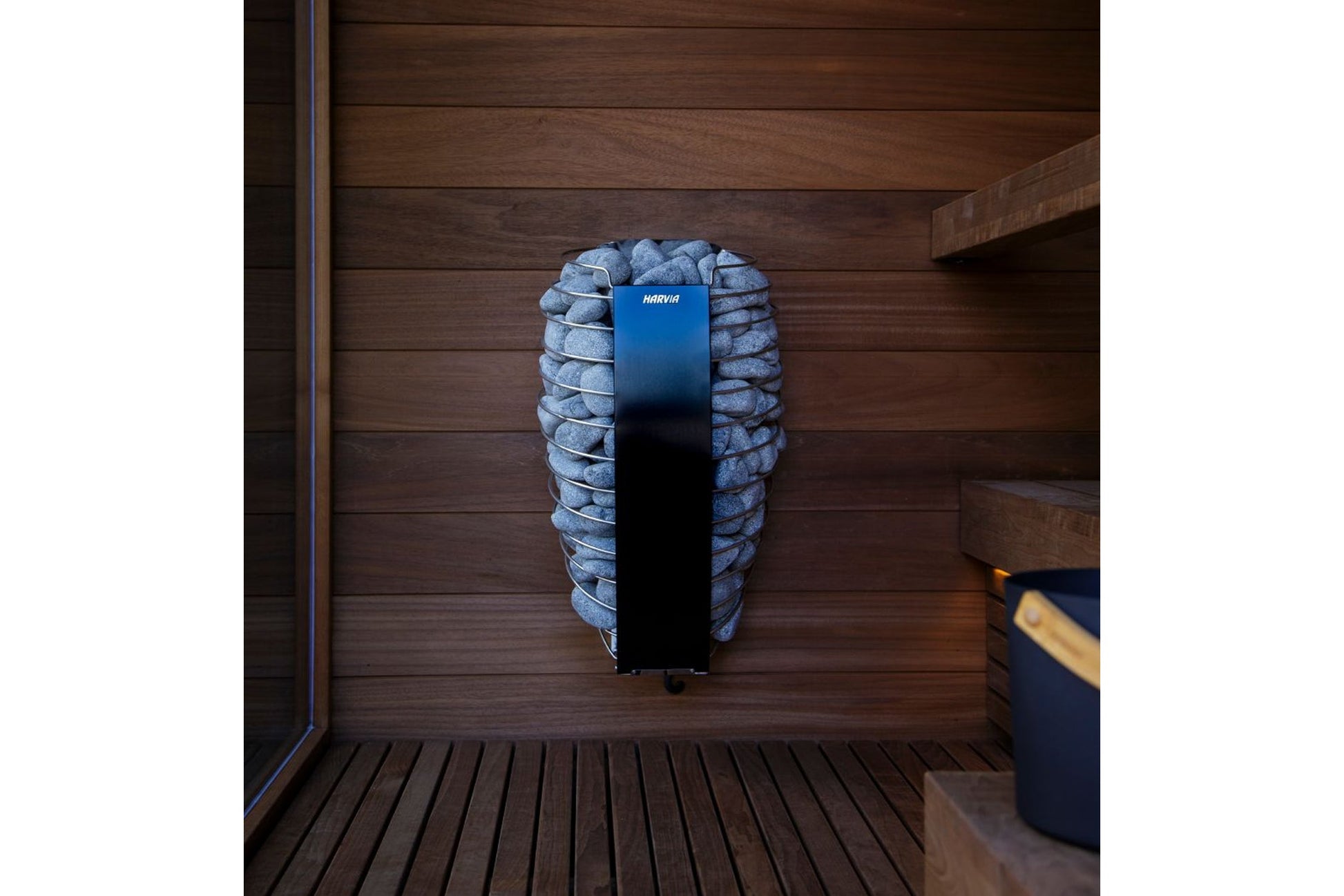 Harvia Spirit electric sauna heater with blue metal casing mounted on wooden sauna wall surrounded by grey stones
