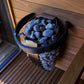Harvia Spirit electric sauna heater with black metal housing and blue stones, displayed on wooden deck with white flowers
