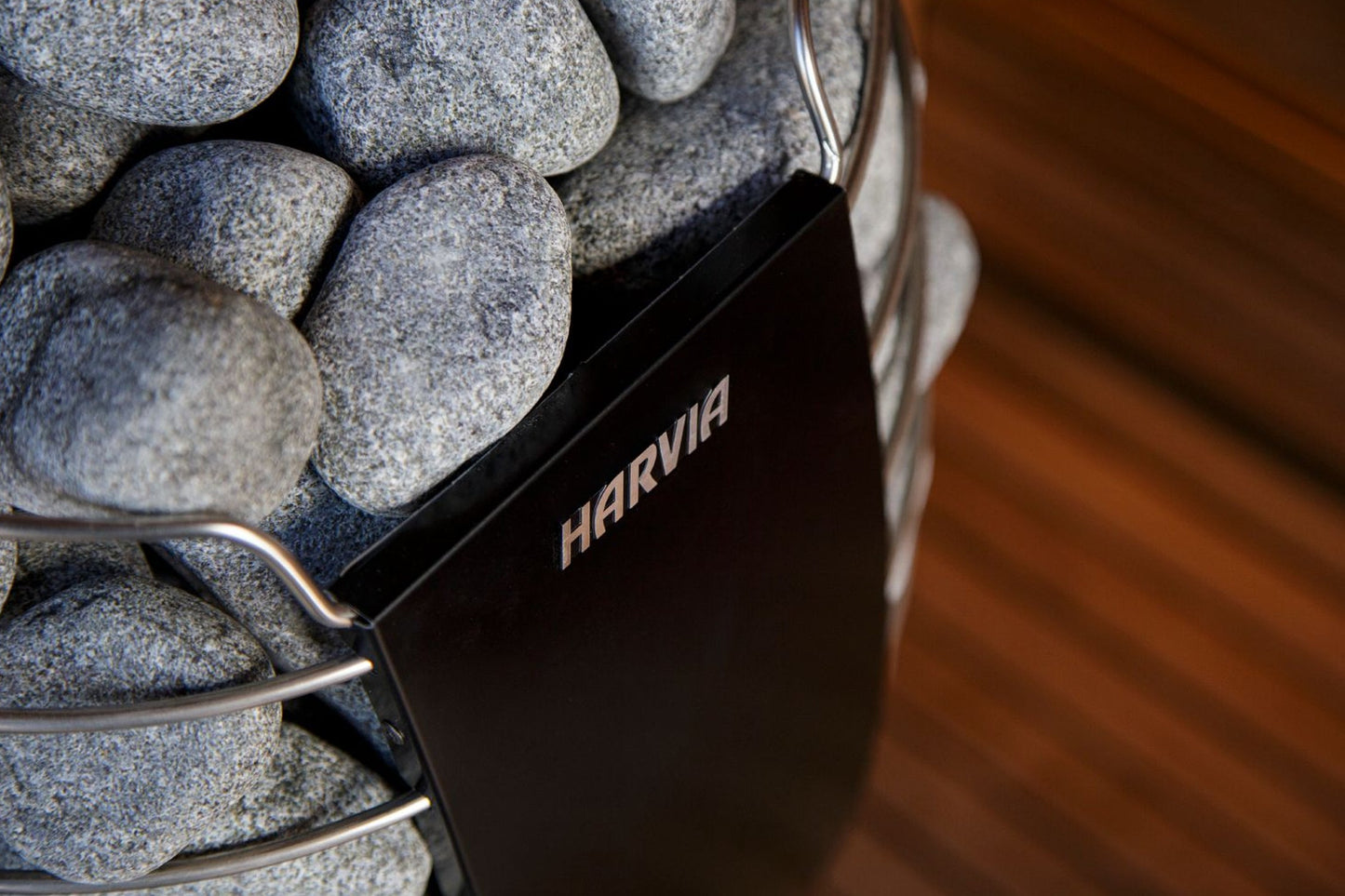 Harvia Spirit sauna heater with gray stones in metal basket, black control panel visible, on wooden background