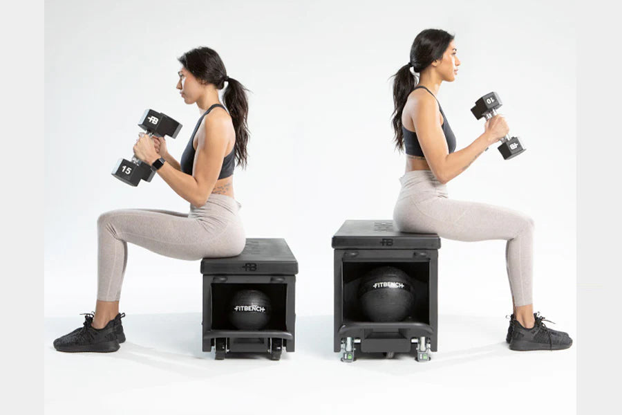 Two women performing dumbbell exercises on black FITBENCH STUDIO weight benches, wearing sports bras and leggings on white ba