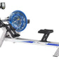FluidRower E520 commercial fluid rowing machine with blue resistance wheel, black seat, digital monitor, and white base on wh