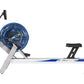 FluidRower E520 Evolution commercial fluid rower with blue resistance drum, white aluminum frame, black foot pedals and handl