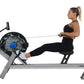 Woman using black and gray FluidRower E550 rower machine with blue flywheel, demonstrating rowing motion