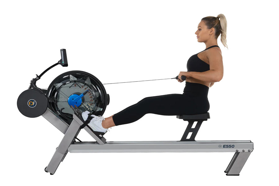 Woman using black and gray FluidRower E550 rower machine with blue flywheel, demonstrating rowing motion