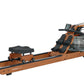 Brown wooden fluid rower with black footrest and seat, water tank resistance mechanism, on white background