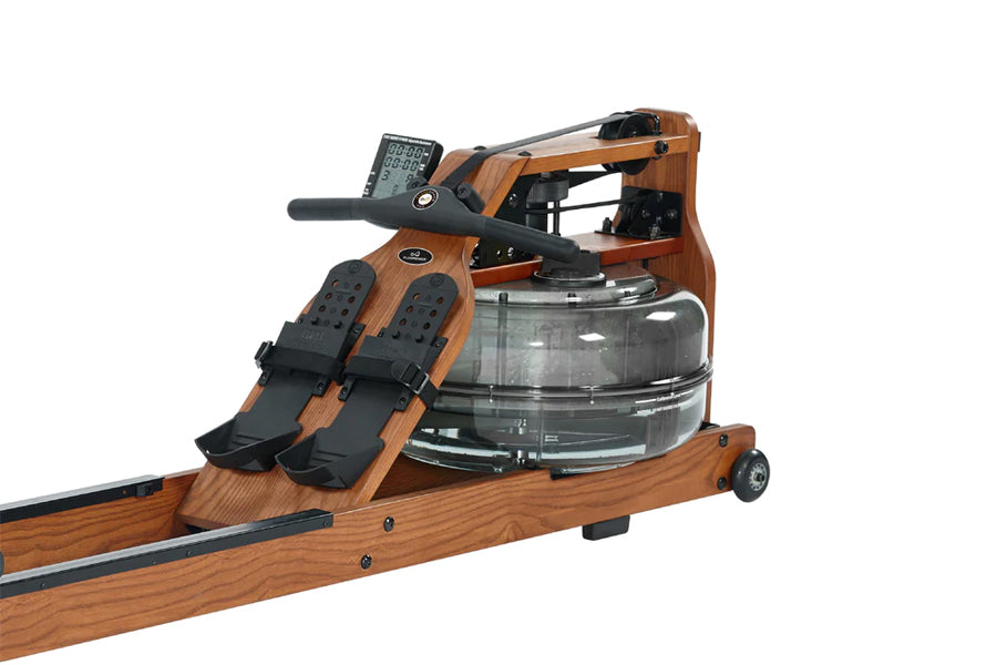Brown wood and black rowing machine with digital monitor, water tank, and padded foot pedals on white background
