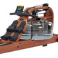 Wood-grain brown fluid rower with black digital monitor, footrests, and clear water resistance chamber on white background