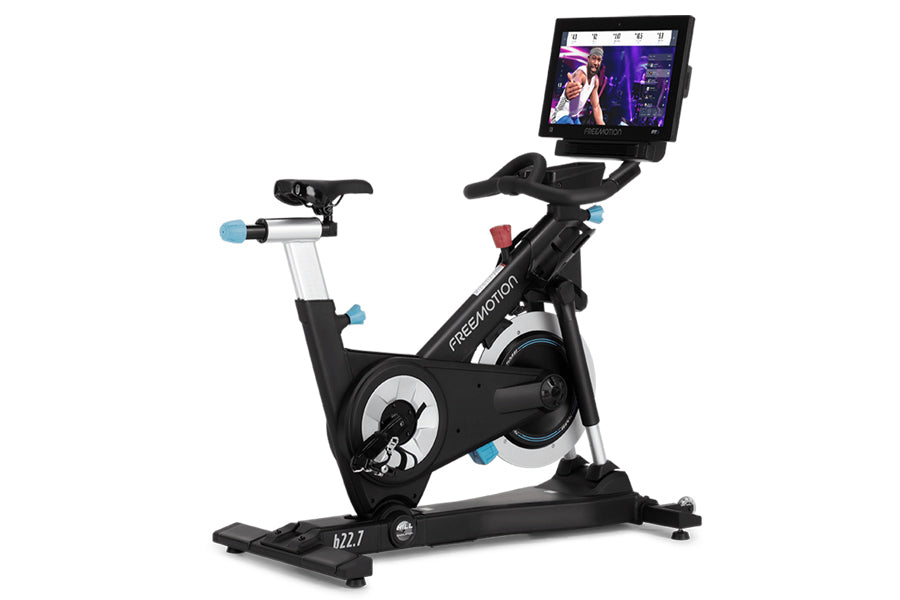 Black and blue stationary exercise bike with tablet display showing fitness class, on white background