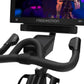 Freemotion CoachBike indoor cycle with black padded handlebars, seat, and base, Freemotion monitor displaying fitness content
