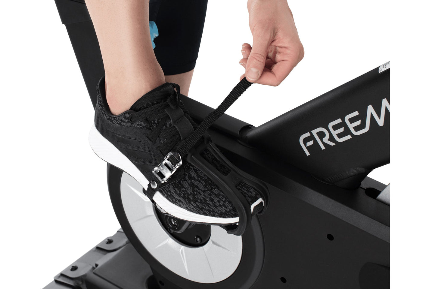 Black and white Freemotion stationary bike pedal with foot strap, worn by model on exercise bike