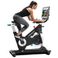 Woman exercising on black and white Freemotion CoachBike indoor cycle with tablet mounted on handlebars displaying fitness co