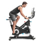 Man in black tank top and gray shorts riding black Freemotion stationary exercise bike with digital display on white backgrou