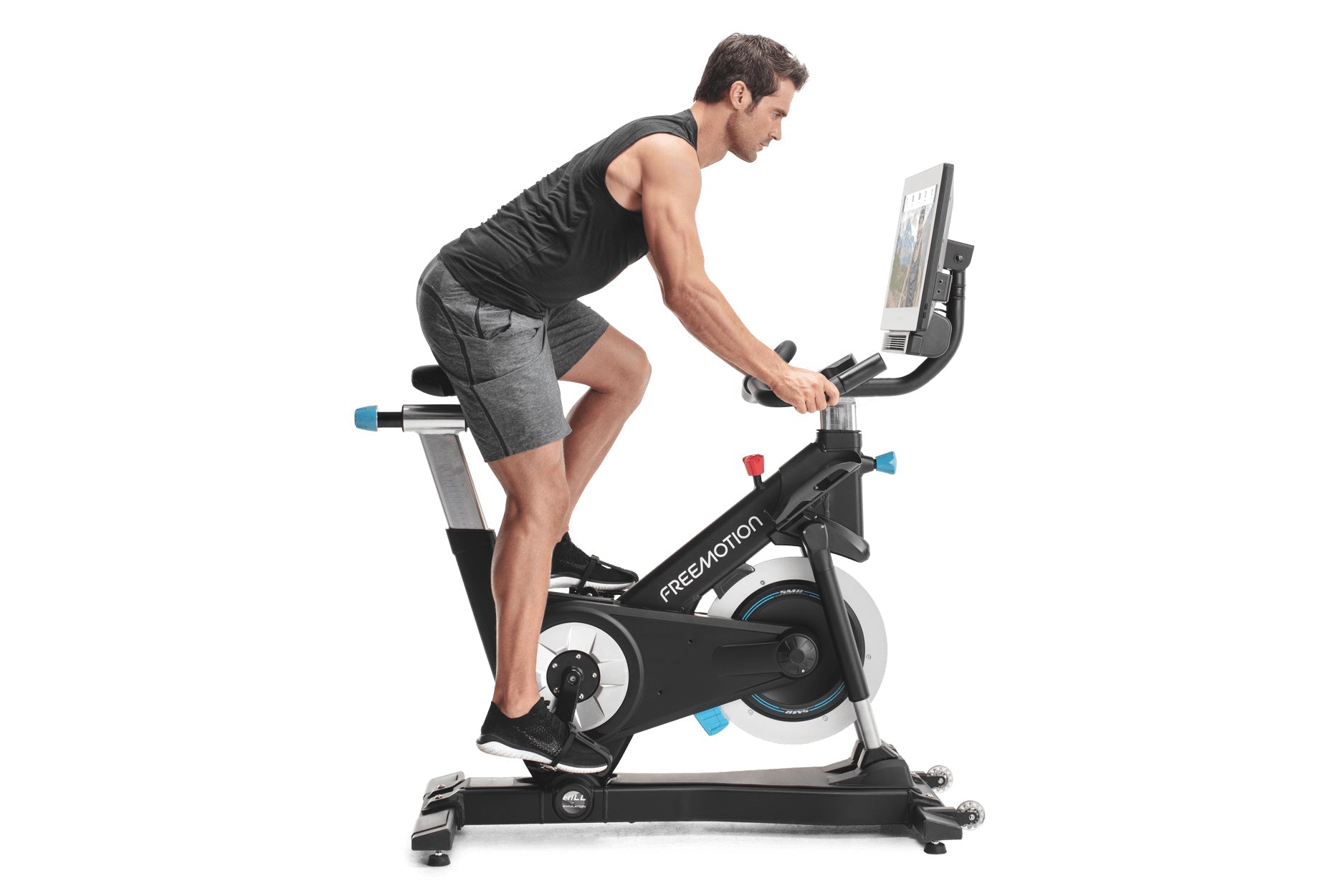 Man in black tank top and gray shorts riding black Freemotion stationary exercise bike with digital display on white backgrou