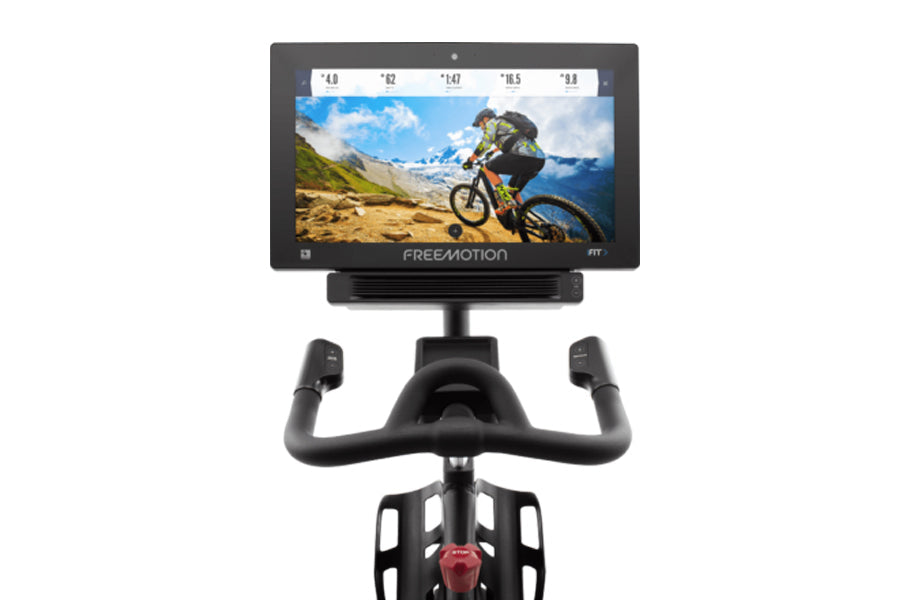 Freemotion CoachBike indoor exercise bike with black frame, curved handlebars, and mounted digital display screen showing mou