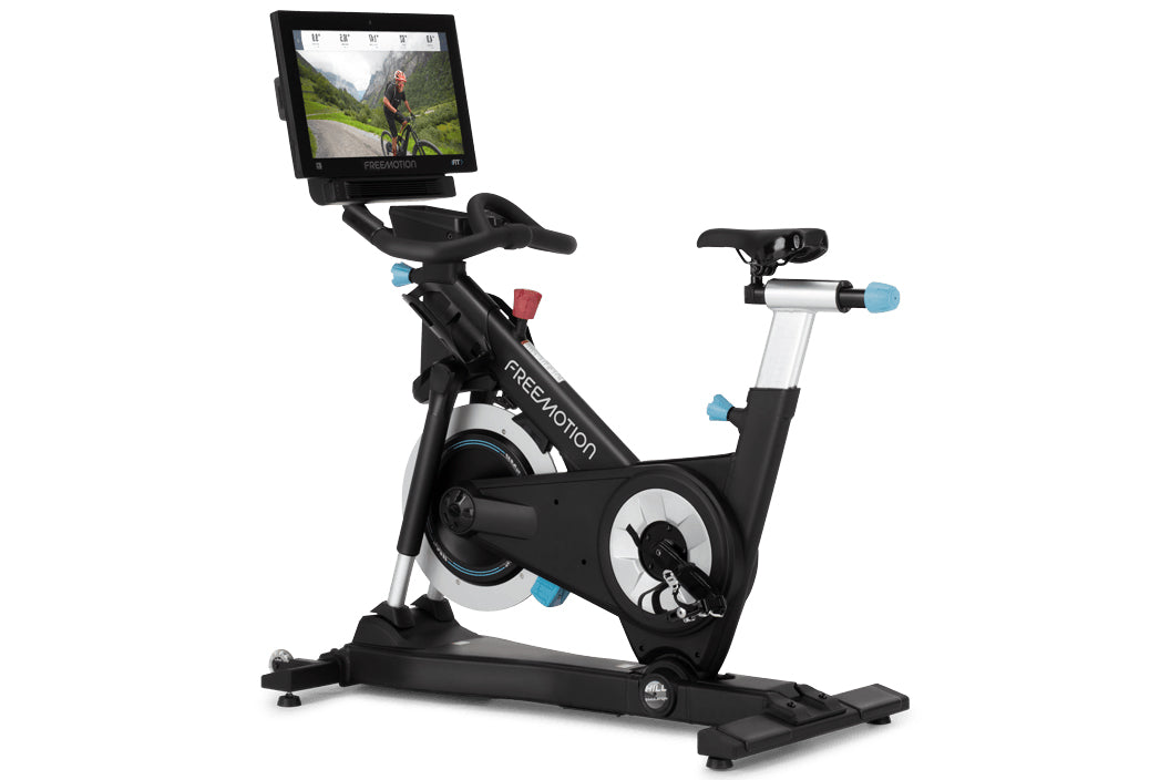 Black and white stationary exercise bike with blue accents, digital screen display mounted on articulating arm, flat pedals, 