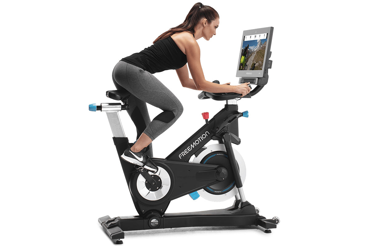 Woman exercising on black and white Freemotion stationary exercise bike with tablet screen mounted, wearing black tank top an