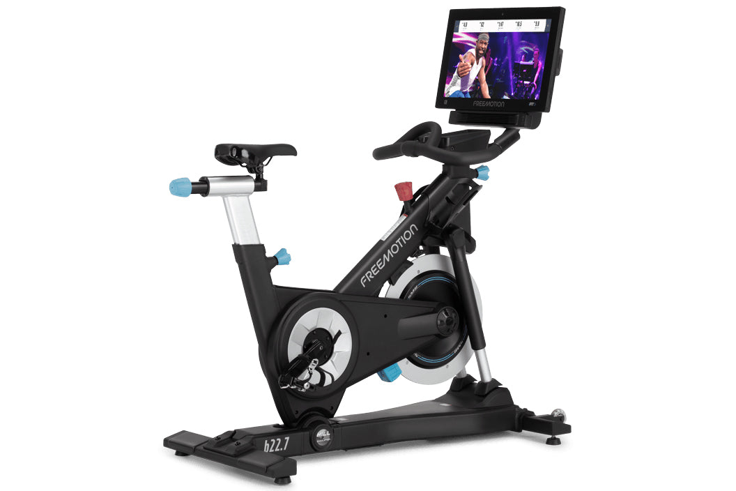 Black and silver Freemotion CoachBike stationary cycle with blue accent grips, attached touchscreen display showing video con