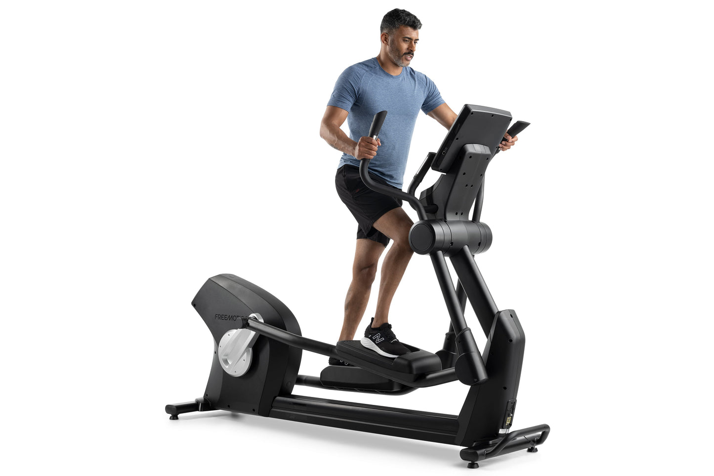 Man wearing blue t-shirt and black shorts using black Freemotion e10.9b elliptical machine with digital display on white back