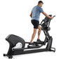 Man wearing blue t-shirt and black shorts using black Freemotion elliptical machine on white background