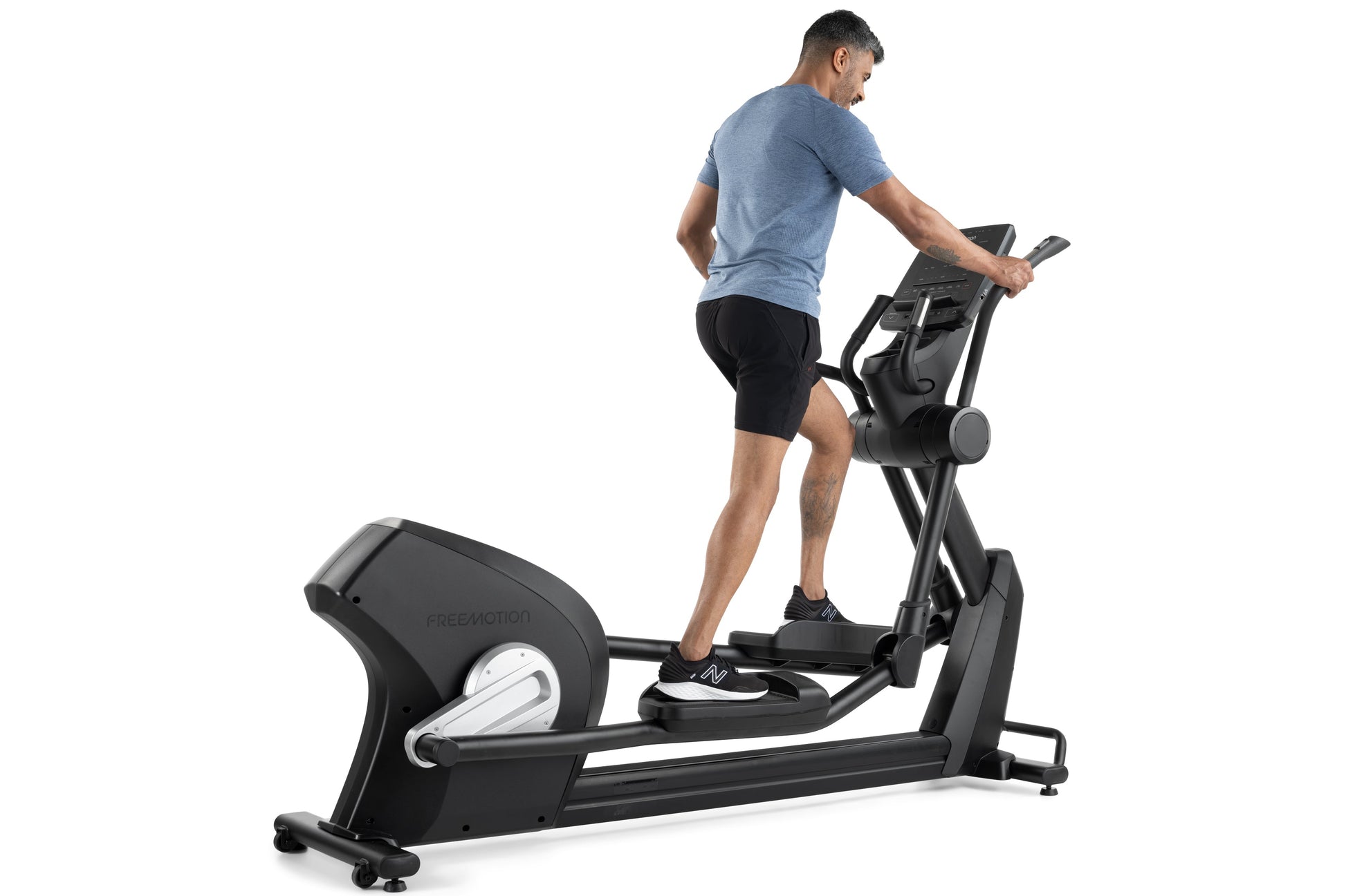 Man wearing blue t-shirt and black shorts using black Freemotion elliptical machine on white background