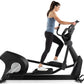 Woman using black Freemotion elliptical machine with blue tank top and black leggings on white background