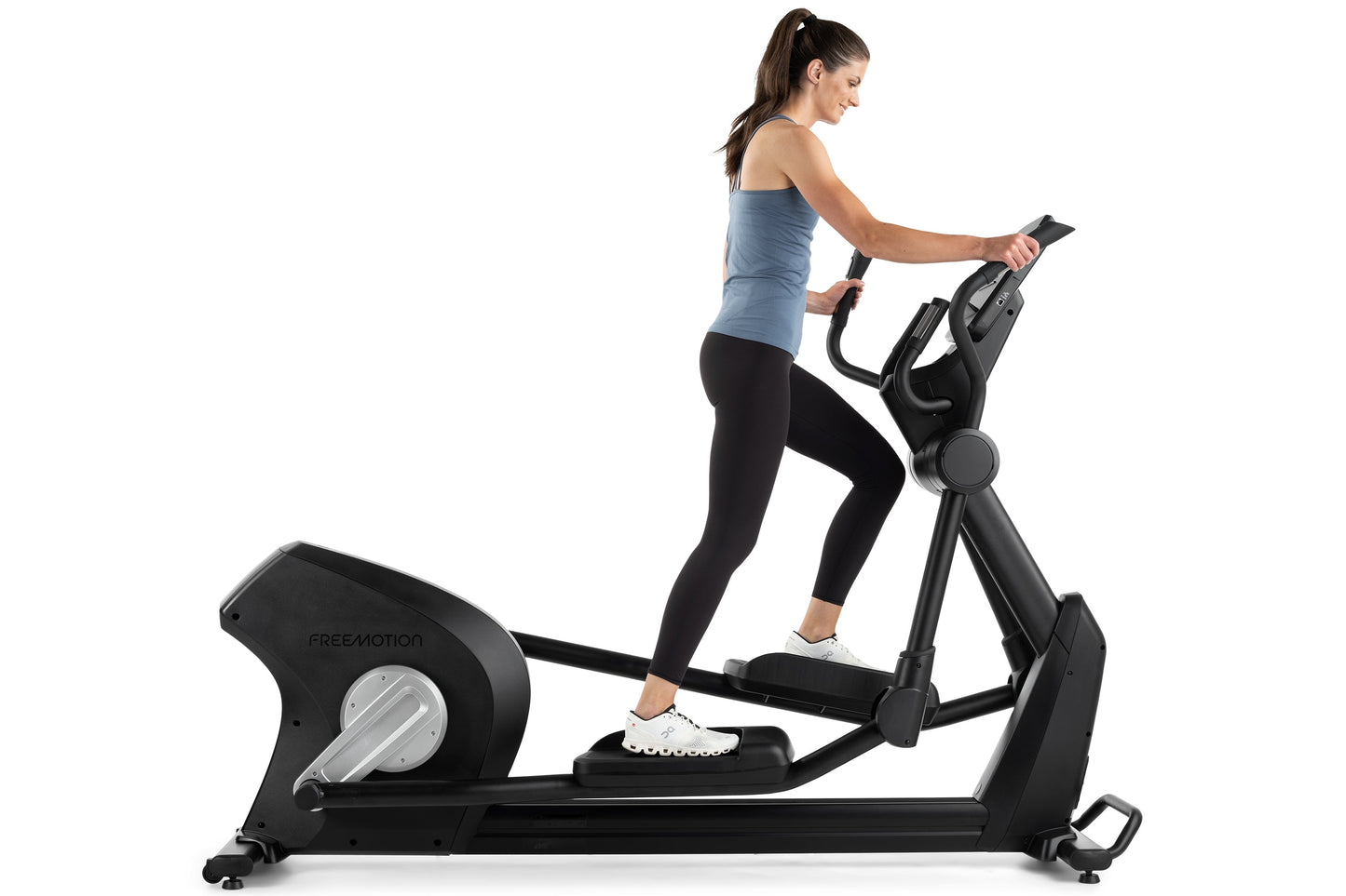 Woman using black Freemotion elliptical machine with blue tank top and black leggings on white background