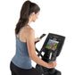 Woman in blue tank top using Freemotion e10.9b elliptical machine with display screen showing workout video, side view on whi
