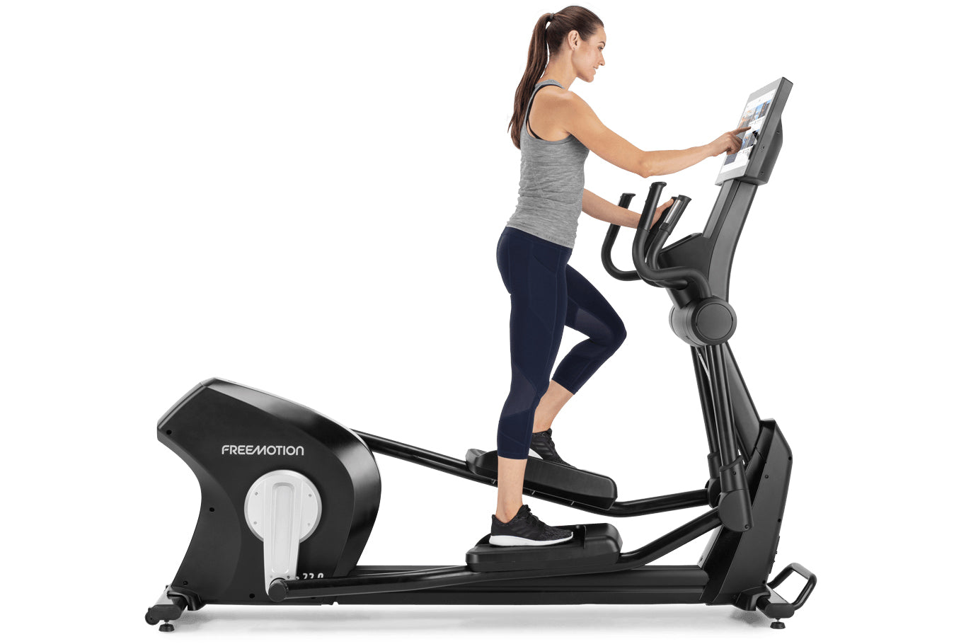 Woman using black Freemotion e22.9 elliptical machine with digital display, worn by model on white background