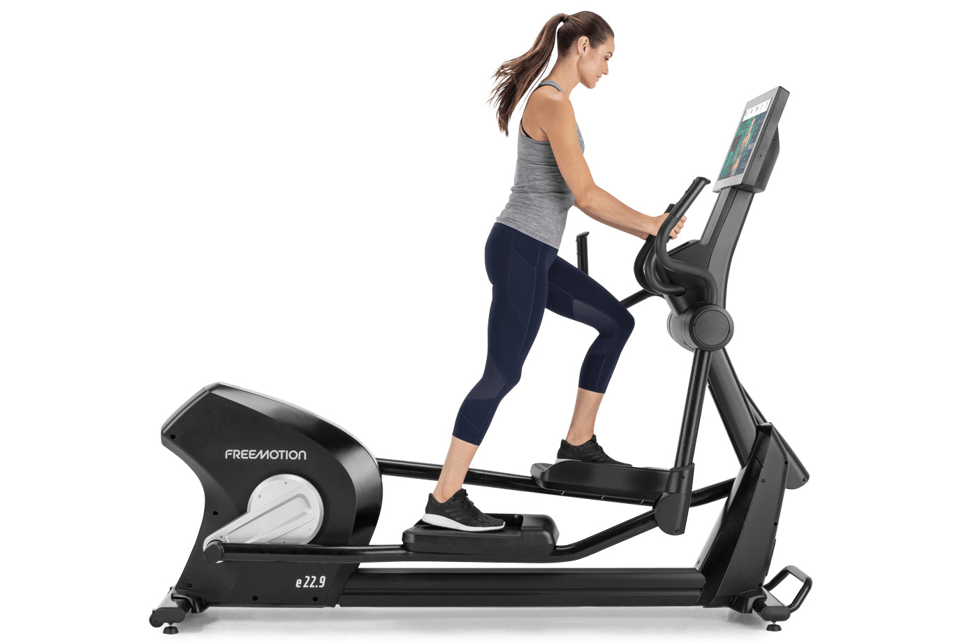 Woman using black Freemotion e22.9 elliptical with digital display, wearing gray tank top and navy capri leggings