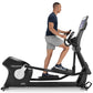 Man wearing navy t-shirt and gray shorts using black Freemotion e22.9 elliptical machine with digital display on white backgr