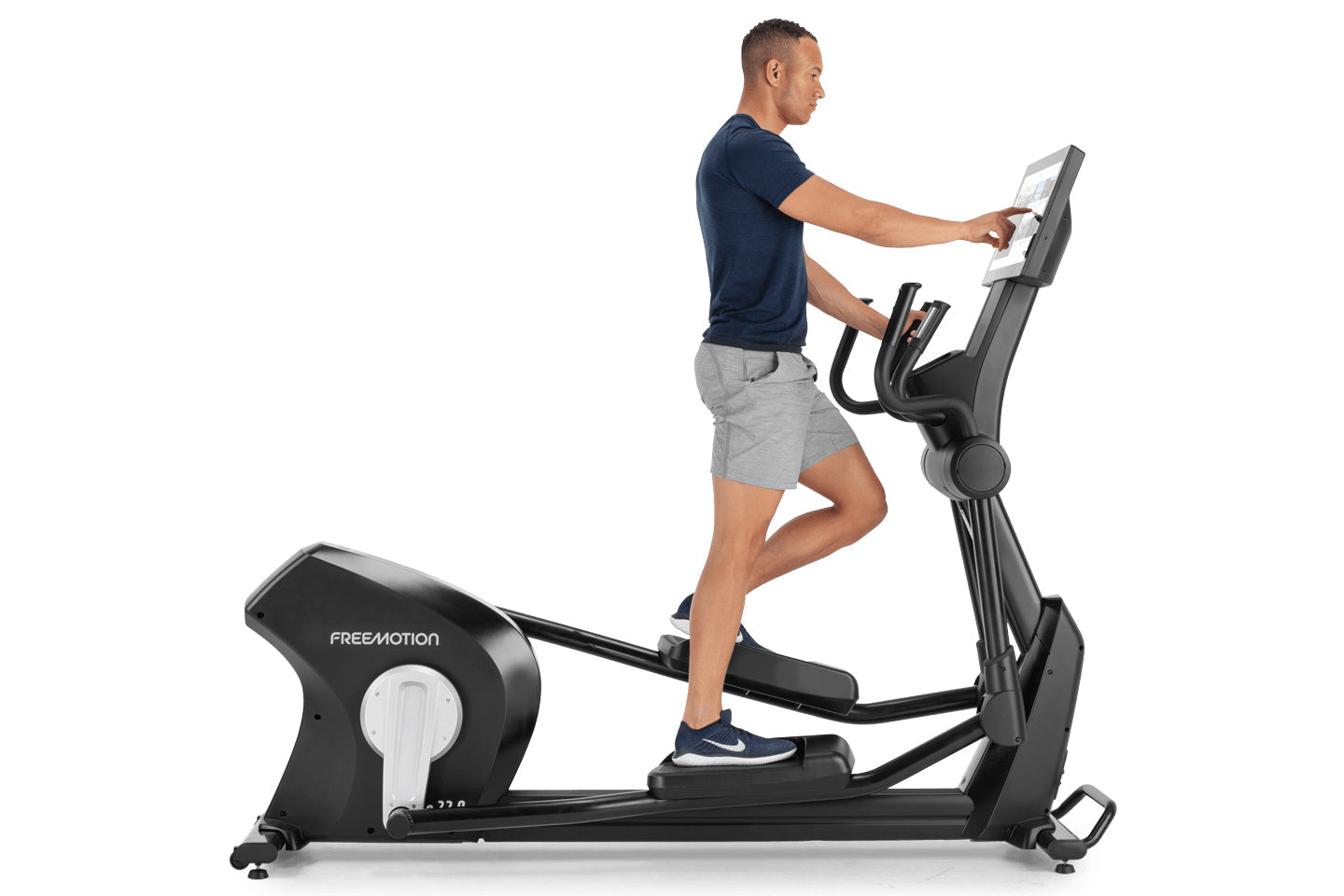 Man using black Freemotion elliptical machine with digital display, wearing navy t-shirt and gray shorts on white background