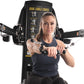 Woman using black Freemotion Genesis Dual Cable Cross machine with dual cable handles extended outward, on white background