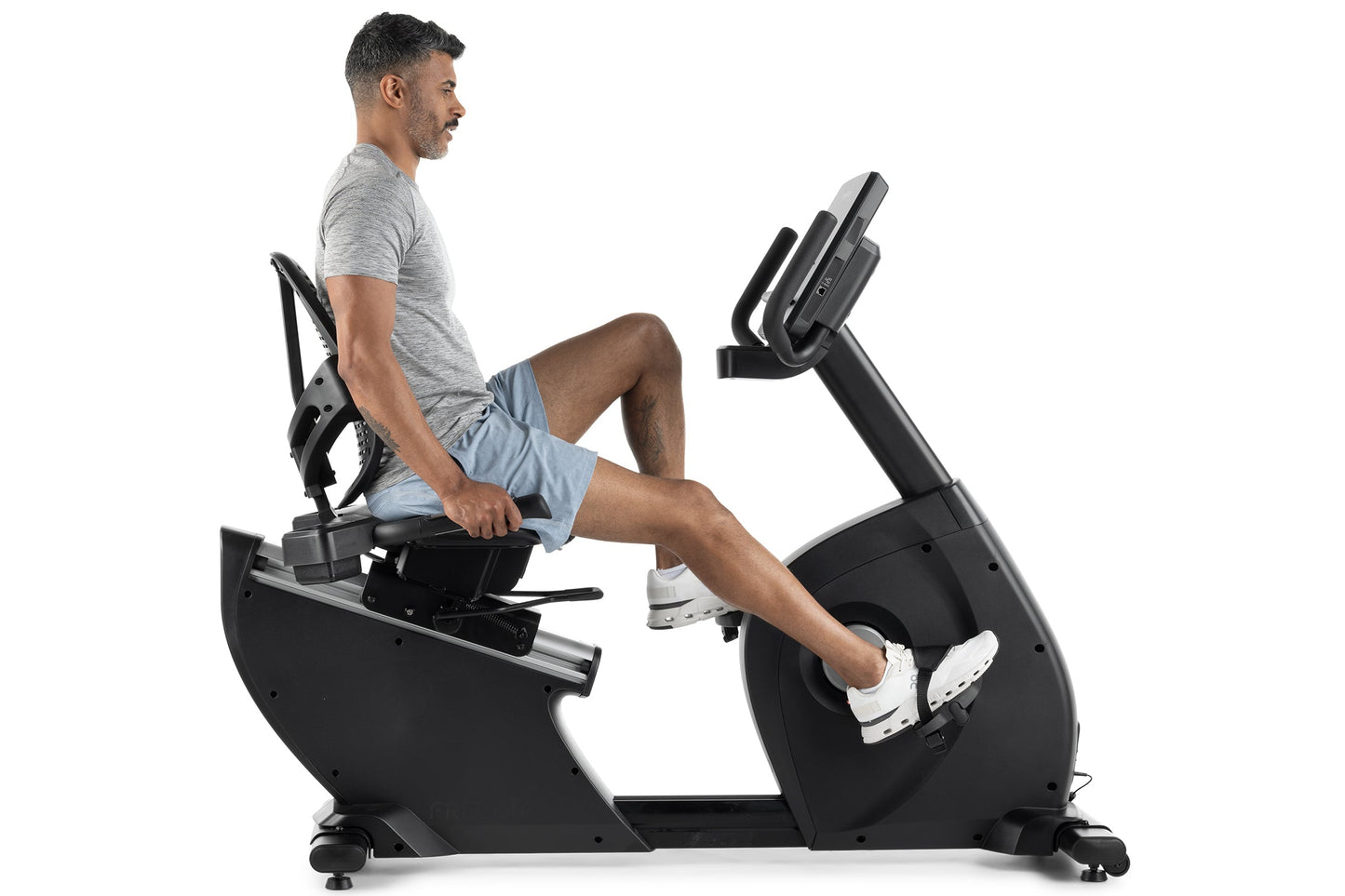 Man in gray shirt and blue shorts using black recumbent exercise bike with digital display on white background