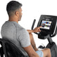 Man using black Freemotion recumbent exercise bike with touchscreen display showing workout content, worn by model on white b