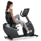 Woman exercising on black Freemotion recumbent stationary bike with digital display, wearing gray leggings and black sports t