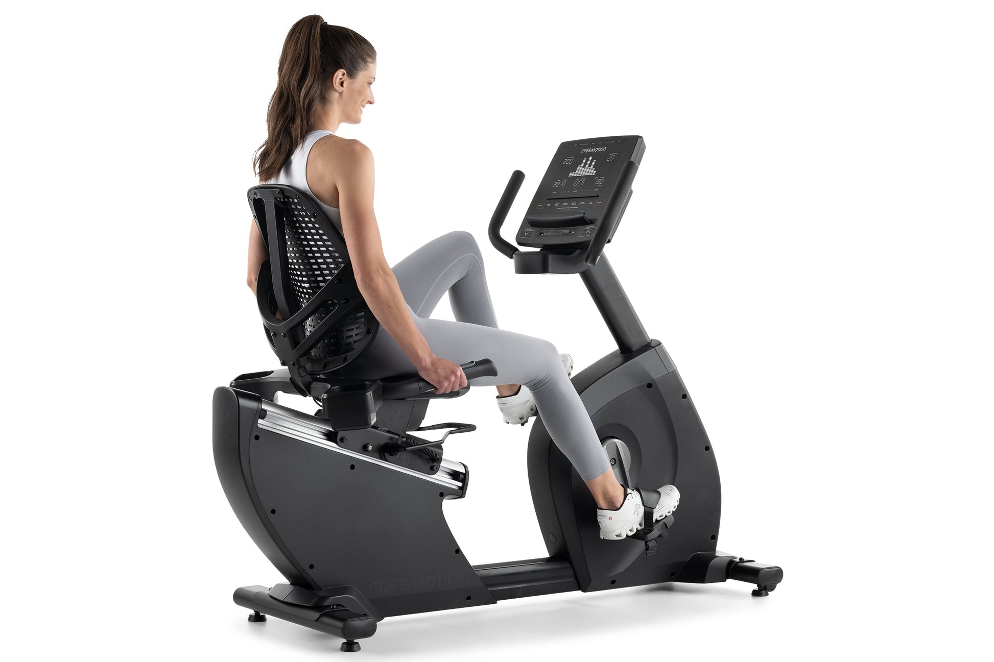 Woman exercising on black Freemotion recumbent stationary bike with digital display, wearing gray leggings and black sports t