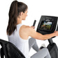 Woman using FreeMotion recumbent exercise bike with digital display showing outdoor biking video, worn white tank top and gra