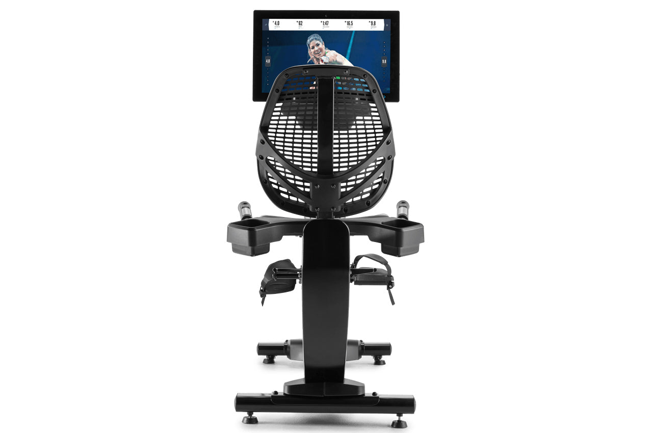 Black recumbent exercise bike with mesh backrest, foot pedals, and mounted tablet display showing fitness content, front view