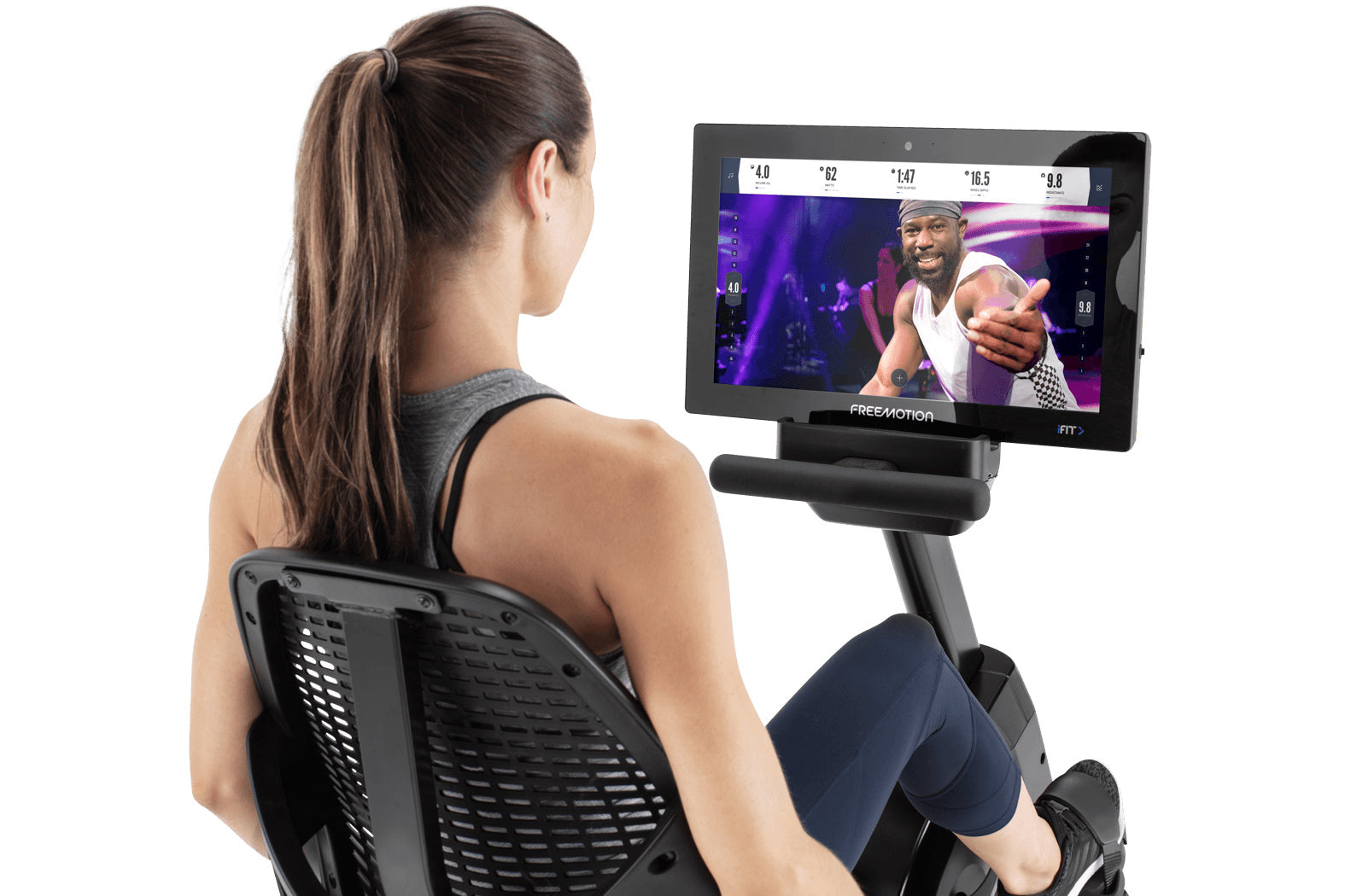 Woman using Freemotion R22.9 recumbent exercise bike with digital display screen showing fitness metrics and instructor